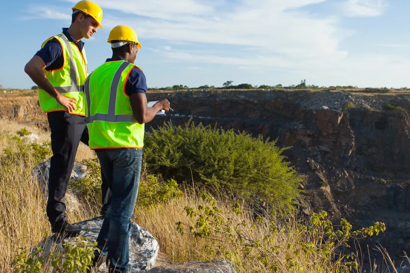 Two workers in safety vests surveying a canyon edge